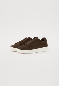 Brown suede sneakers with a rounded toe, featuring flat laces, a cushioned collar, and a white rubber sole.