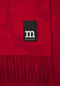 Red wool blanket with a soft texture, featuring fringed edges and a black label with white lettering displaying "marimekko."