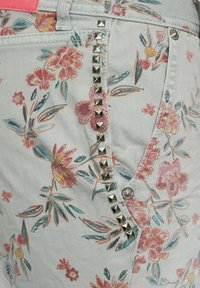 Denimshorts med blommönster i ljusblått med rosa och gröna accenter. Har metalliska nitar längs sidan och en silverfärgad knappdetalj.