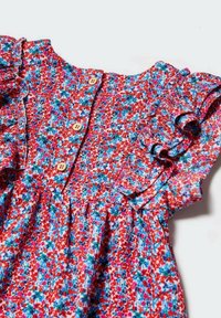 Kwiatowa sukienka w czerwone, niebieskie i białe wzory, z falbaniastego rękawami i drewnianymi guzikami przy dekolcie. Teksturowana tkanina z plisami.