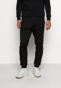 Pantalon de jogging noir en tissu doux, avec une coupe ajustée, une taille élastique et des poches latérales ornées d'un logo discret.