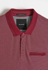 Bordowa koszulka polo wykonana z tkaniny o fakturze; posiada dopasowany krój, trzy guziki, płaski kołnierzyk oraz małą kieszonkę z przeszytym brzegiem.