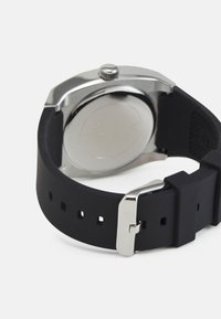Correa de reloj de silicona negra con hebilla de metal, caja de acero inoxidable y respaldo metálico liso. Presenta un diseño minimalista y ajuste ajustable.