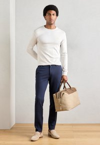 Lichtbeige lange mouwen shirt, marineblauwe op maat gemaakte broek, tan suède loafers en een beige sporttas met bruine accenten. Gladde texturen overal.