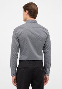 Langemouwige shirt van zwart-wit gestreept stof. Heeft een klassieke kraag en knoopmanchetten, gecombineerd met zwarte broek.