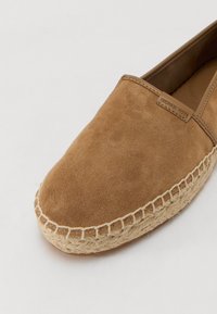 Barna velúr slip-on cipő fonott jútatalppal és egy kis dombornyomott logó címkével. Simafa felület, kerek orrdesign.
