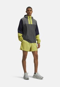 Herreur vest i grå med gule detaljer og navy ærmer, parret med matchende gule shorts og grå træningssko.