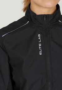 Schwarze, leichte Jacke mit hohem Kragen, ausgestattet mit einem Reißverschluss vorne, reflektierenden Akzenten und dem Text "ELITE LAB" in Weiß an der Seite.