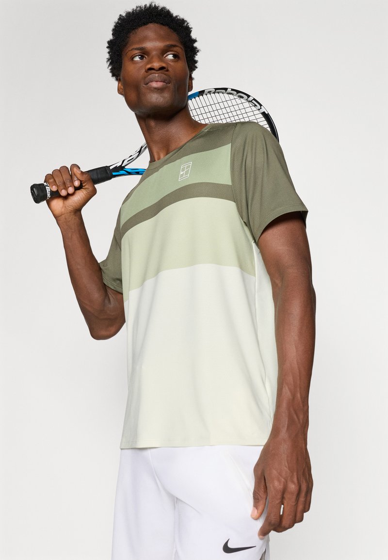 Short-sleeve athletic shirt in light green and beige, featuring horizontal stripes, moisture-wicking fabric, and a small logo on the chest.