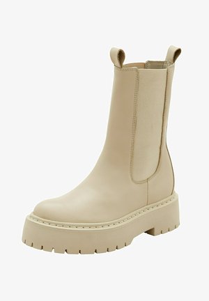 Bottine en cuir beige avec des panneaux latéraux élastiques, bout rond et semelle en caoutchouc épaisse dotée d'un profil texturé pour une meilleure adhérence.