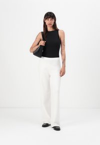 Zwarte geribbelde tanktop, witte wijde broek, zwarte handtas en zwarte loafers. Gladde stof en strakke lijnen. Minimalistisch ontwerp.