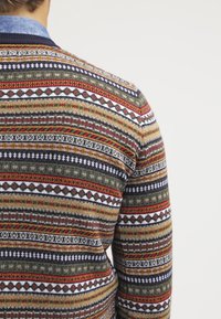 Pull en tricot avec un motif multicolore comprenant des rayures et des motifs géométriques en rouge, vert, marine et blanc. Tissu texturé.