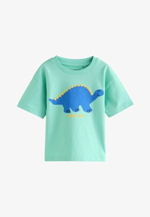 T-shirt verde chiaro a maniche corte con grafica di un dinosauro blu con spine gialle e il testo "GRANDIO GIORNO" in giallo sottostante.