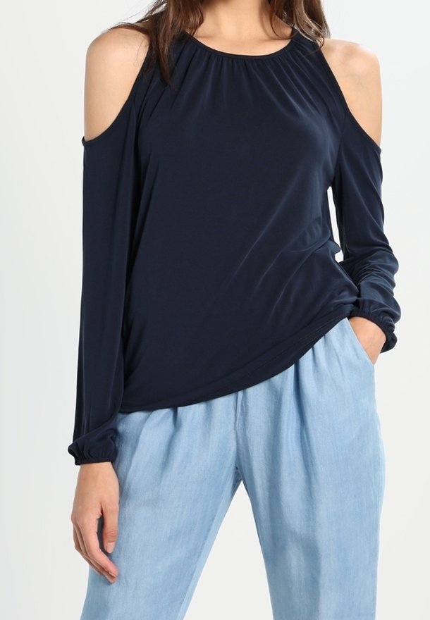 Tmavě modrý top s odhalenými rameny, dlouhými rukávy, nařaseným výstřihem a elastickými manžetami, doplněný světlými volnými kalhotami.
