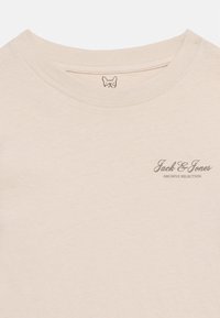 Μπεζ μπλουζάκι με στρογγυλή λαιμόκοψη, με εκτύπωση "Jack & Jones Archive Selection" σε μικρό, γκρι χρώμα στην αριστερή πλευρά του στήθους και μικρό λογότυπο σκύλου στο εσωτερικό γιακά.