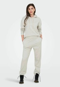 Hellgrauer Hoodie mit passenden Jogginghosen, ausgestattet mit einer Kordelzugkapuze und Seitentaschen, kombiniert mit schwarzen Schnürstiefeln. Glatte Textur.