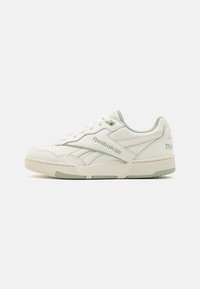 Nízké tenisky Reebok v off-white a světle zelené barvě, s tkaničkami, logem značky na boku a texturovanou podrážkou, zobrazené z vnější strany.