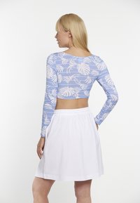 Svetlomodrý krátky crop top s dlhým rukávom a bielym vzorom listov, nosený s bielou sukňou s elastickým pásom. Výrez na chrbte odhaľuje pokožku.