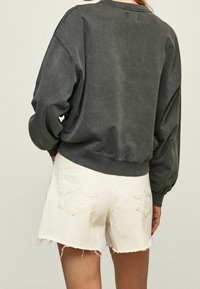 Sudadera corta de color gris oscuro con hombros caídos y puños acanalados, combinada con pantalones cortos blancos desgastados que presentan una costura decorativa en el bolsillo.