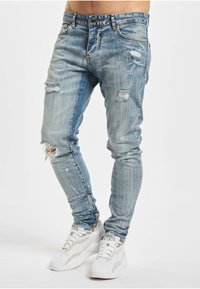 Lyseblå denimjeans med smal passform, med flere slitte partier og frynsete kanter. Brukes sammen med hvite joggesko.