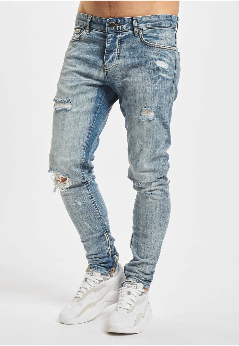 Lyseblå denimjeans med smal passform, med flere slitte partier og frynsete kanter. Brukes sammen med hvite joggesko.