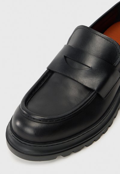 Mustad mustad nahast loafers, millel on sile tekstuur, tikitud serv ja pehme riba ülevalt. Paks, sooniline kummitald.