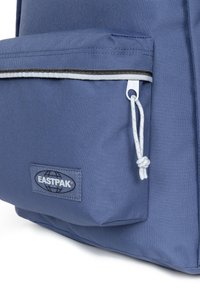 Modrý batoh EASTPAK má přední kapsu s bílým šňůrkovým uzávěrem, černým lemováním a nášivkou s logem. Odolná tkanina s hladkou texturou.