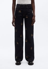 Tumedast teksast laiade säärega teksapüksid, millel on punaste ja kollaste kroonimotiividega tikandid üle kogu pinna. Sirge lõikega siluett, kitseneva vöökoha ja kontrastsete õmblustega.