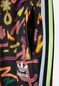 Svarta träningsbyxor med livfulla, flerfärgade abstrakta mönster, dragkedjeficka och Adidas trefoil-logga i vitt nära fållen.