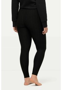 Leggings noirs texturés avec un motif en grille, coupe ajustée et taille haute, adaptés pour une tenue décontractée ou des séances d'entraînement. Modèle pieds nus présenté.