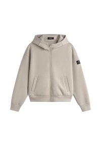 Sudadera con cremallera de color beige claro, con bolsillos frontales, mangas largas, capucha y una pequeña etiqueta negra en la parte superior de la manga izquierda.