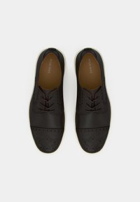 Chaussures en cuir noir à finition lisse, avec des accents perforés, un bout rond et une semelle en caoutchouc blanche. Lacées à l'avant.