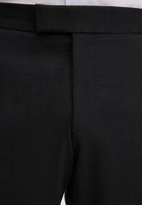 Schwarze Hose mit flacher Front, ausgestattet mit einem sauberen Bund, dezent sichtbaren Nahtstichen und einer glatten Textur ohne Taschen.