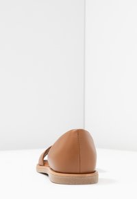 Zapato plano de cuero marrón claro con un diseño abierto, que presenta una puntaredondeada y una suela texturizada. Estilo simple y minimalista.