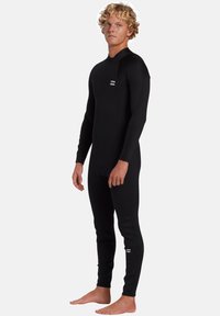 Mutino nero realizzato in materiale elastico, con maniche lunghe e gambe intere. Logo distintivo sul petto e sulla parte bassa della gamba, texture liscia.