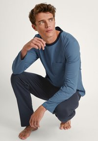 Blauwe lange mouwen shirt met een zwarte kraag en zak, gecombineerd met marineblauwe broek. Zachte stof, ontspannen pasvorm en minimalistisch ontwerp.