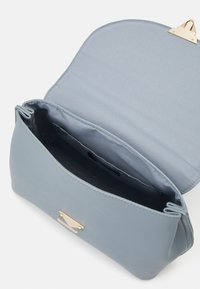 Bolso de mano azul claro con un acabado texturizado. Presenta un cierre de tono dorado y un interior espacioso forrado con tela a juego.