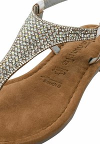 Tan mockask thong-sandal med silverdetaljer och en sträng dekorerad med kristaller. Mjuk fotbädd erbjuder komfort; har "Touch it"-märke på undersidan.