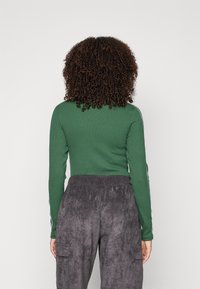 Grön ribbade långärmad topp med vita sidofickor, kombinerad med grå texturerade joggers med cargo-fickor och elastisk midja.