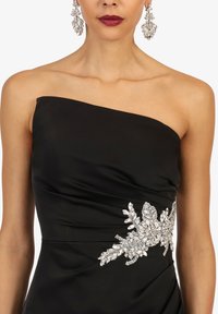Robe noire sans bretelles avec des embellissements floraux en cristal argenté à la taille, portée avec des boucles d'oreilles en cluster argenté assorties et du rouge à lèvres rouge.