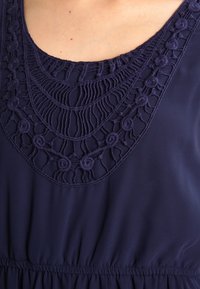 Marinblus med intrikata broderade detaljer runt halsringningen, med samlat tyg vid midjan för en lätt volangeffekt.