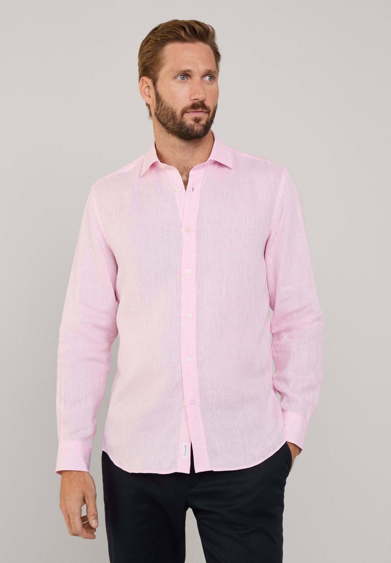 Camisa de manga larga rosa claro hecha de una tela texturizada, con un cierre de botones en el frente y un cuello clásico. Combinada con pantalones oscuros.