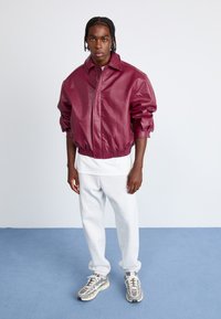 Bordeaux leren bomberjack met een aansluitende elastische zoom en oversized mouwen, gecombineerd met grijze sweatpants en sportieve sneakers.