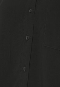 Camicia nera con bottoni, caratterizzata da una texture liscia, con quattro bottoni rotondi neri e una tasca applicata sul lato sinistro.