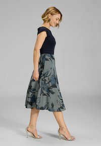 Top ajustado azul marino con mangas cortas y una falda tipo A con movimiento que presenta un patrón floral y rayas en tonos de azul y gris. Sandalias de tacón alto plateadas.