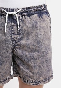 Shorts de bain pour hommes en tissu texturé dans des nuances de bleu et de beige, dotés d'une taille élastique et d'un cordon blanc avec des accents noirs.