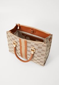 Torba tote w beżowym płótnie z brązowym nadrukiem logo, z brązowym skórzanym paskiem i uchwytami, złotym okuciem i zamkiem błyskawicznym.