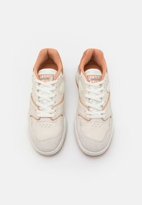 White and peach tennis shoes with a leather and suede upper, round toe, white laces, and a rubber sole. Lacoste logo on the tongue.