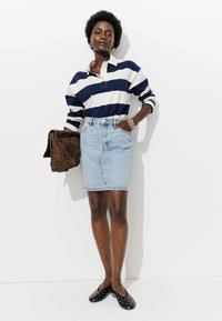 Polo rayé bleu marine et blanc à manches longues, jupe crayon en denim bleu clair, chaussures noires à enfiler avec des clous blancs, et un sac à main en imprimé léopard.