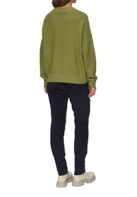 Olijfgroen geribbelde trui met een ontspannen pasvorm, ronde hals en verlaagde schouders, gecombineerd met marineblauwe broek en beige stevige schoenen.